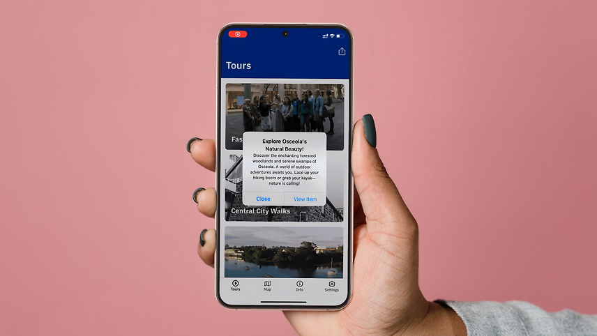 Hand holding smartphone with in-app push notification about Osceola tour on a visitor engagement app.