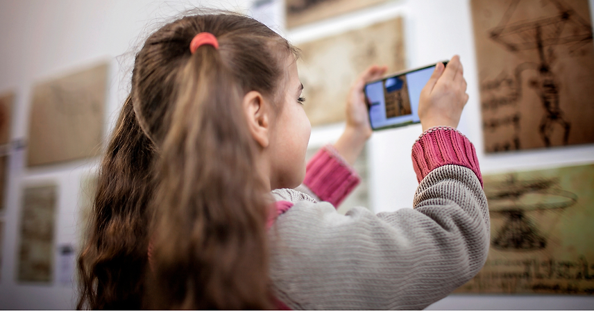 Girl in a museum smiling while using augmented reality on a phone.