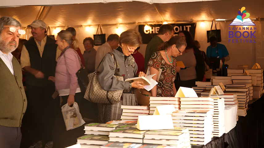 Crowd browsing books under a tent at the Savannah Book Festival with checkout area in background.